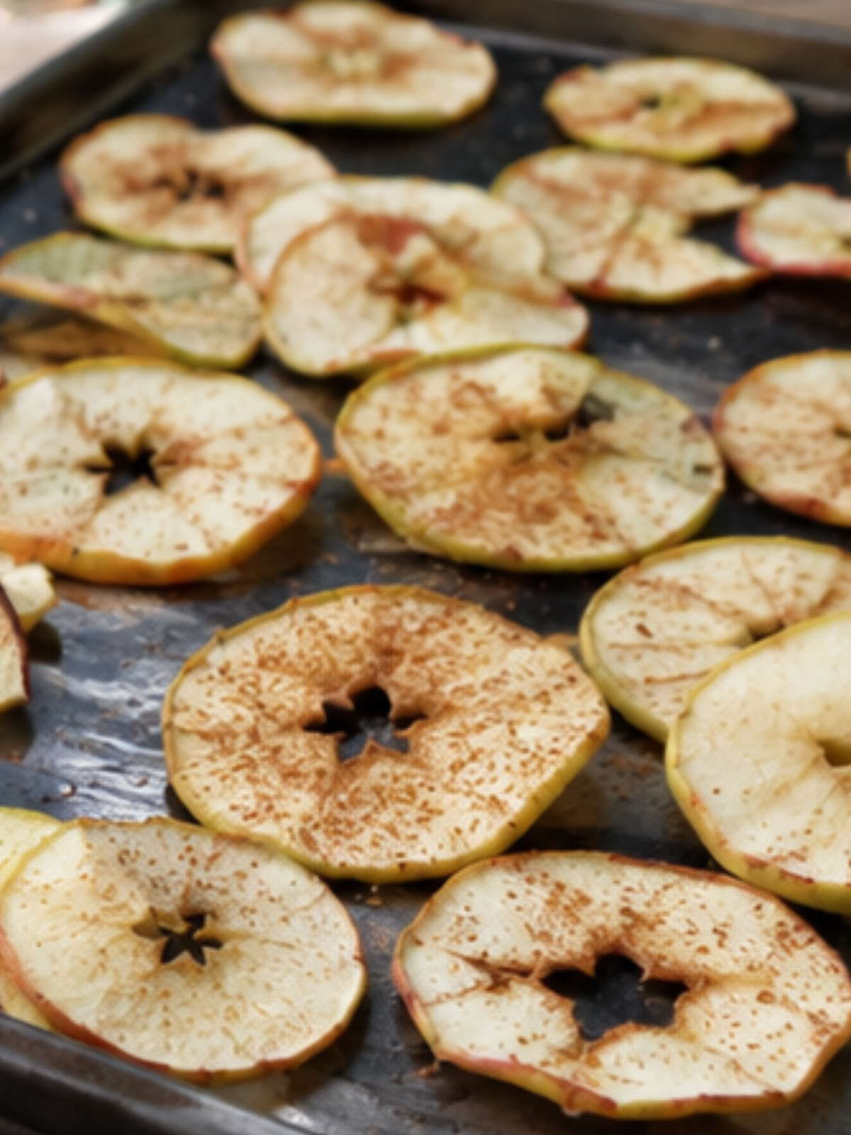 Dünn geschnittene Apfelchips auf einem Backblech mit Zimt. Knuspriger Herbstsnack aus Äpfeln, natürlich getrocknet im Ofen.
