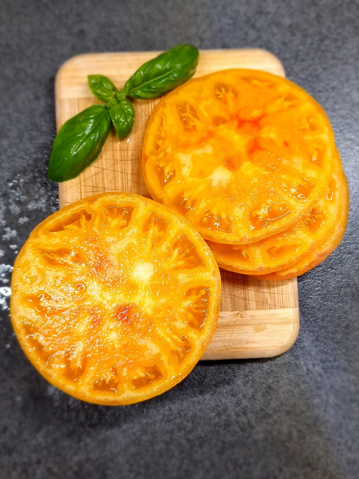 Gelbe Fleischtomate (Buffalo Sun) in Scheiben auf Holzbrett mit Basilikum – aromatische Tomate für Garten und frische Küche